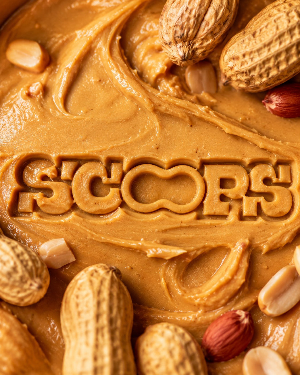 The Scoops wordmark pressed into a swirl of peanut butter, ringed with whole peanuts